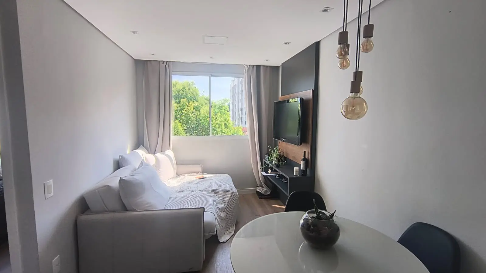 Sala de estar com sofá, mesa redonda e painel de TV